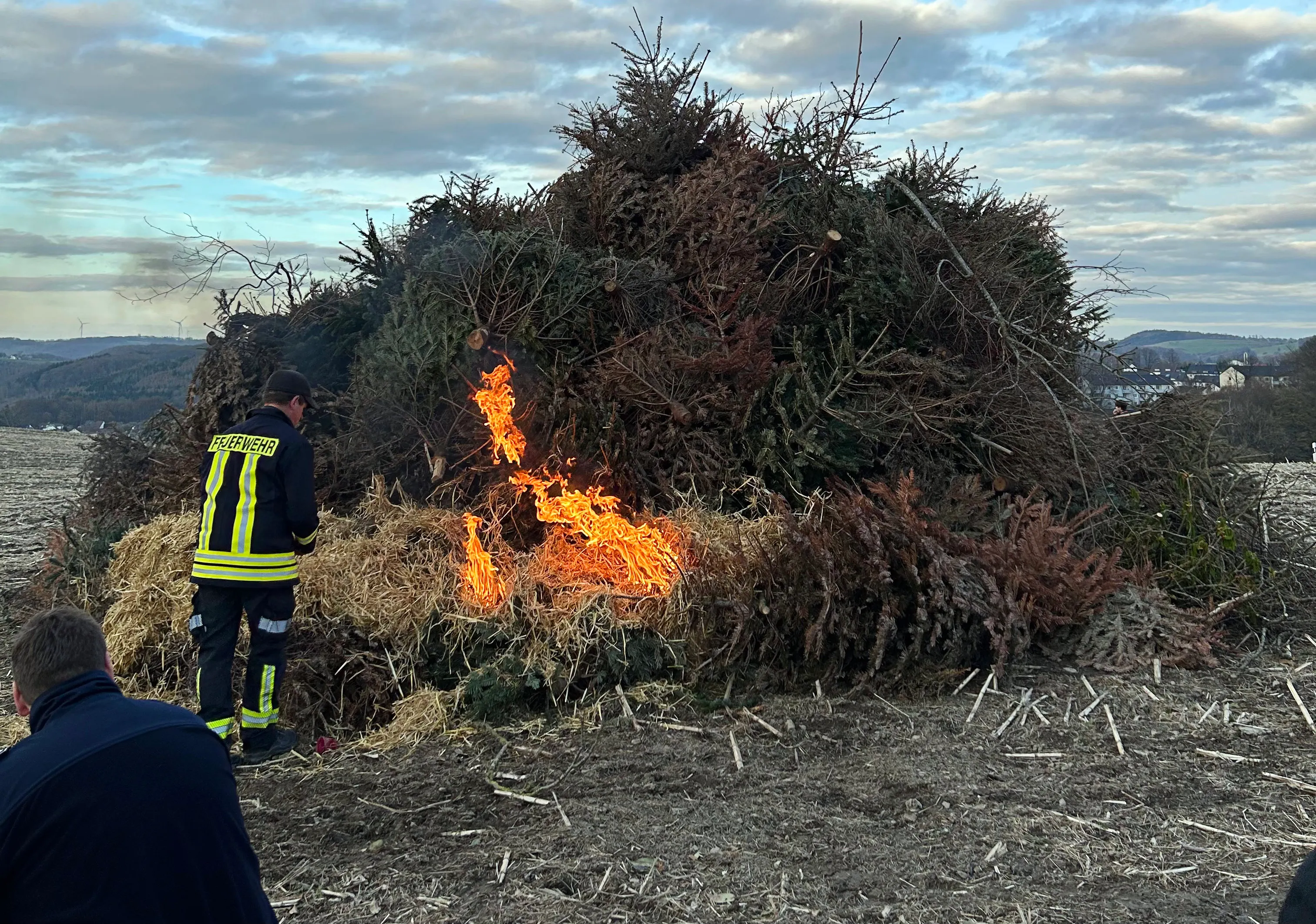 Ein großes Osterfeuer aus Ästen und Reisig brennt auf einem Feld, im Hintergrund eine Hügelkette.