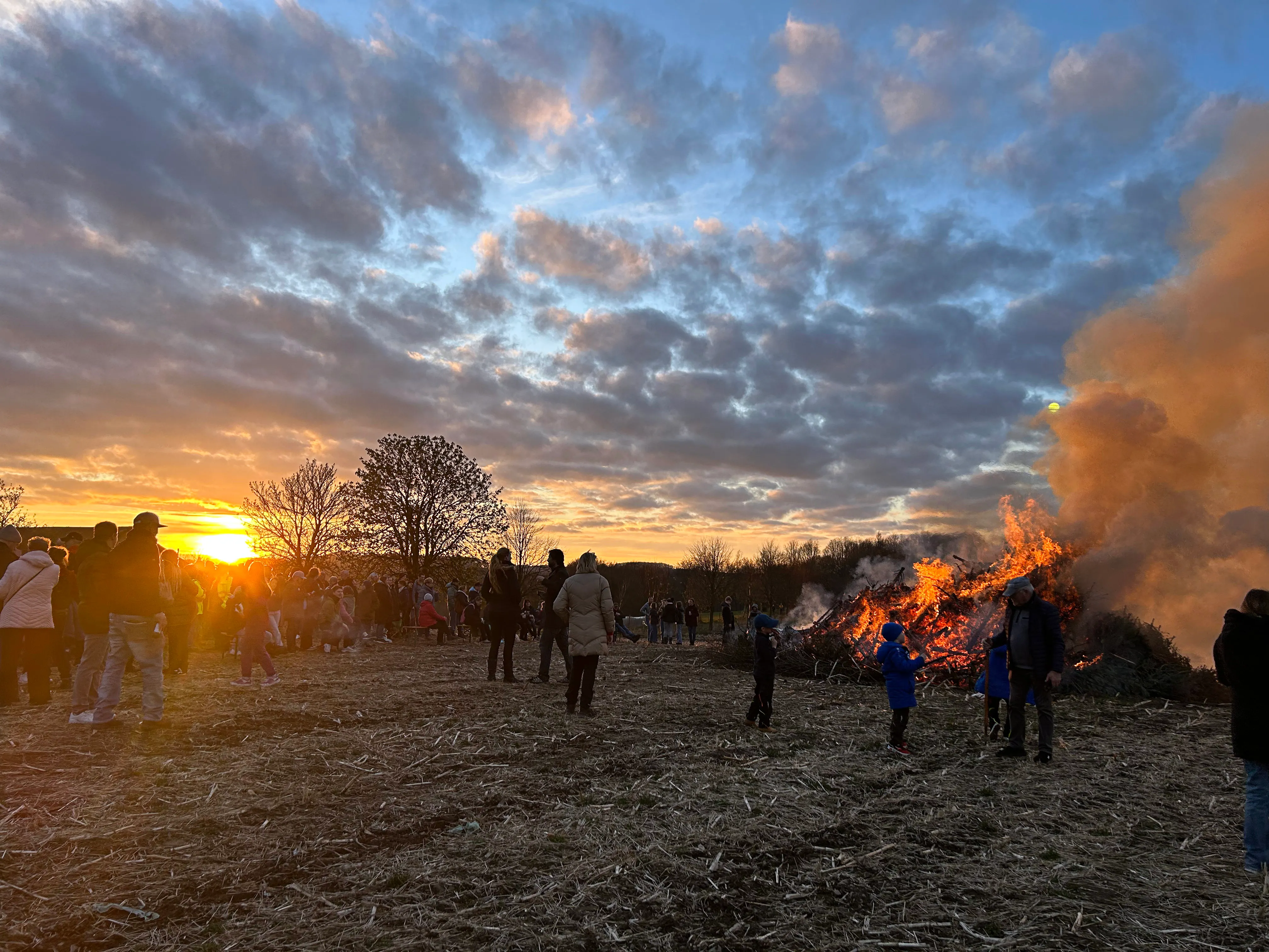 Großes Osterfeuer mit vielen Zuschauern bei Sonnenuntergang auf einem Feld.