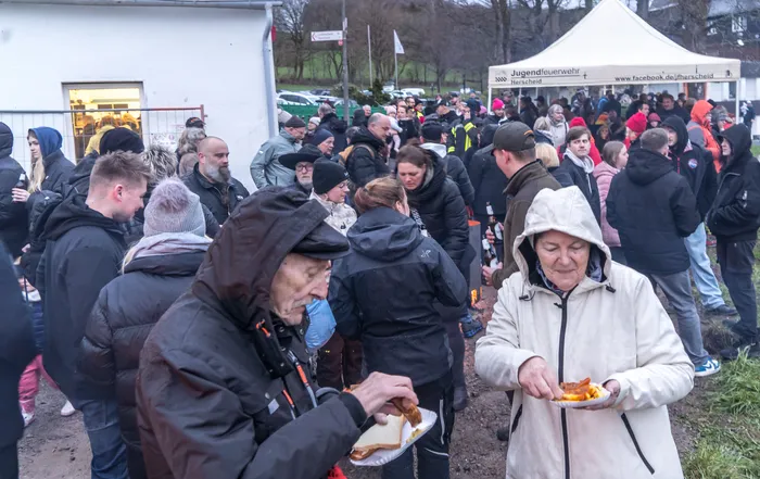 Menschen drängen sich um einen Imbissstand auf dem Herscheider Osterfeuer in Reblin, viele halten Essen in den Händen.