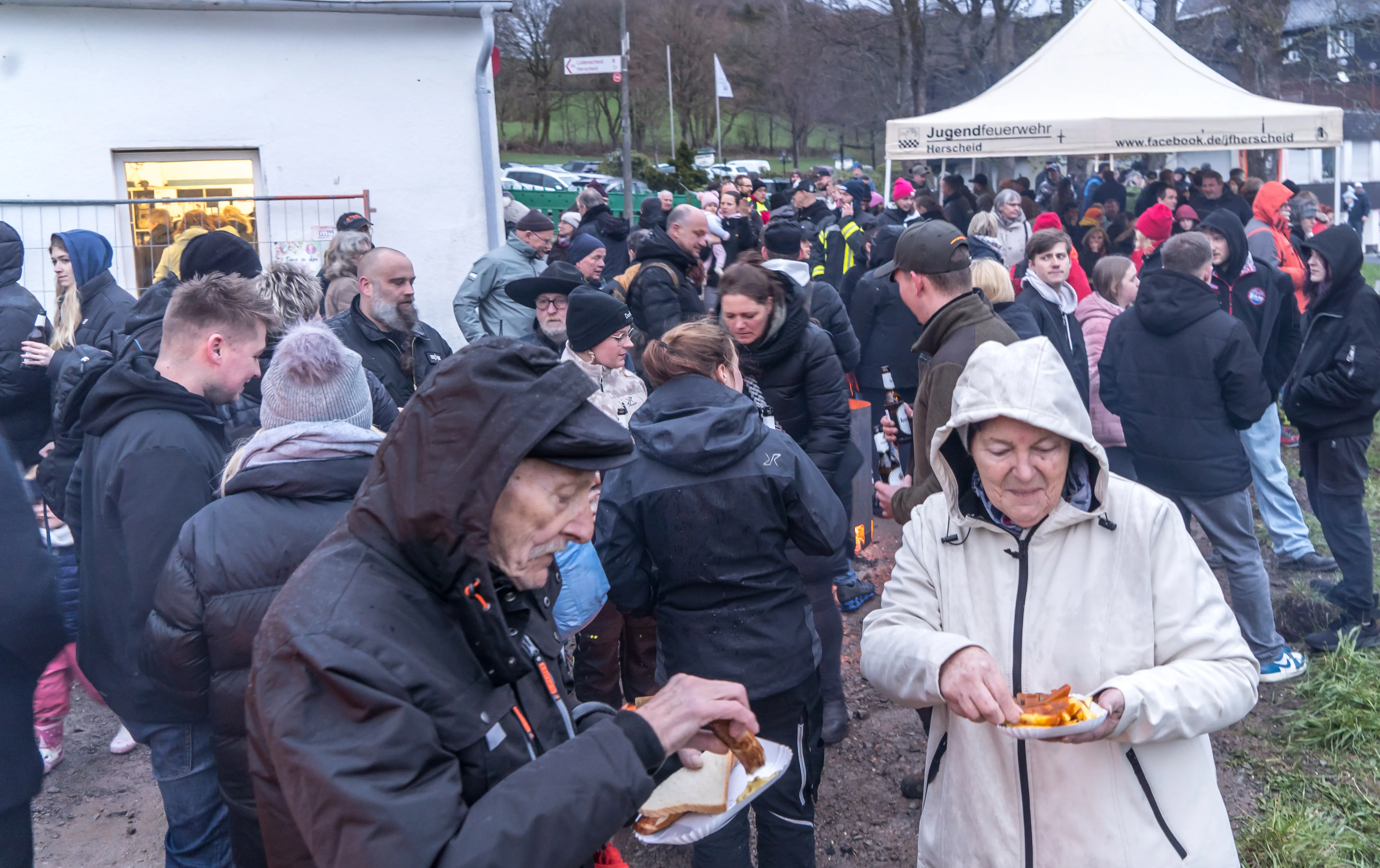 Menschen drängen sich um einen Imbissstand auf dem Herscheider Osterfeuer in Reblin, viele halten Essen in den Händen.
