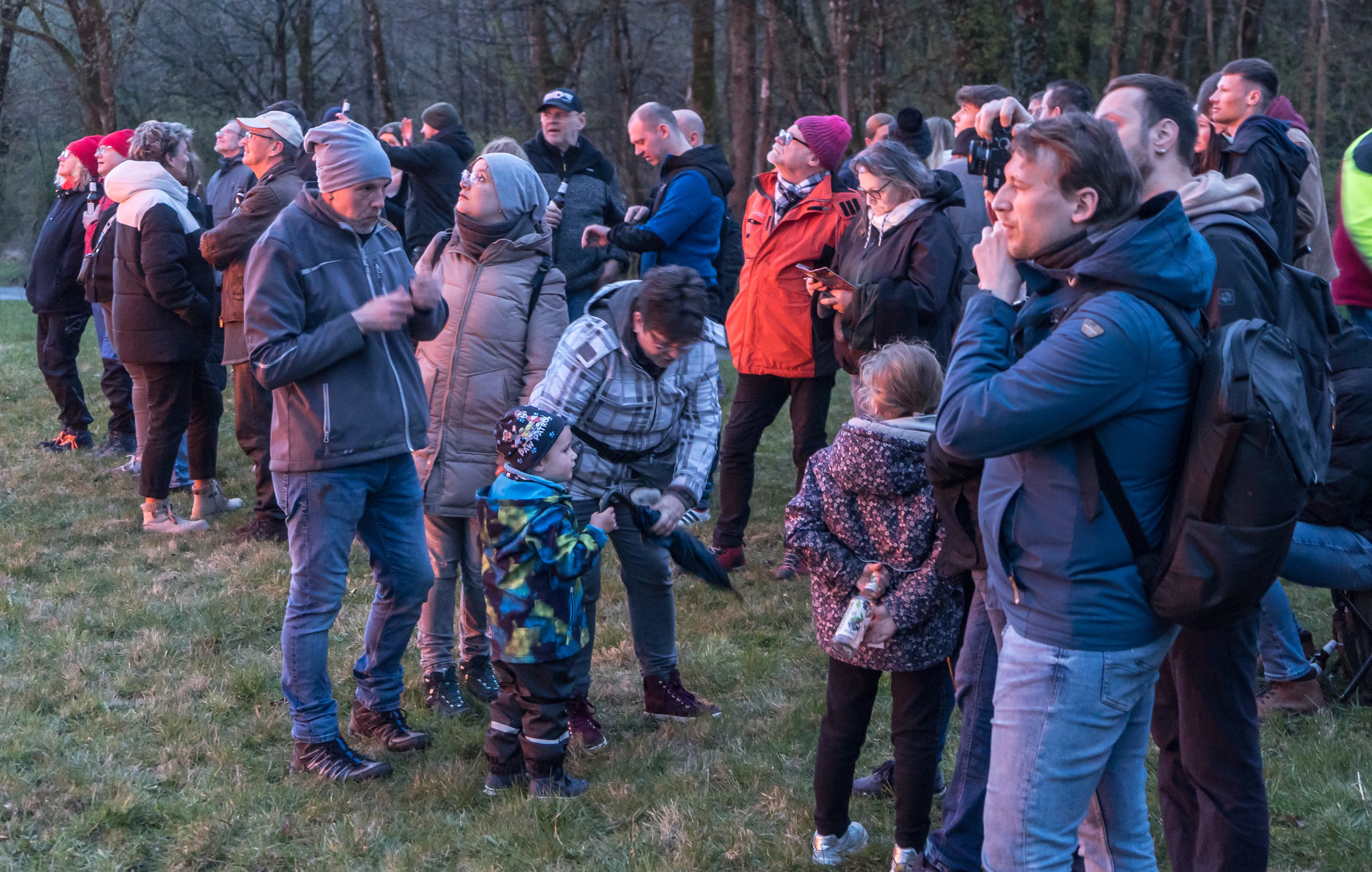 Eine große Menschenmenge steht auf einer Wiese und blickt in Richtung eines Osterfeuers, während ein Kind im Vordergrund von einem Erwachsenen gehalten wird.