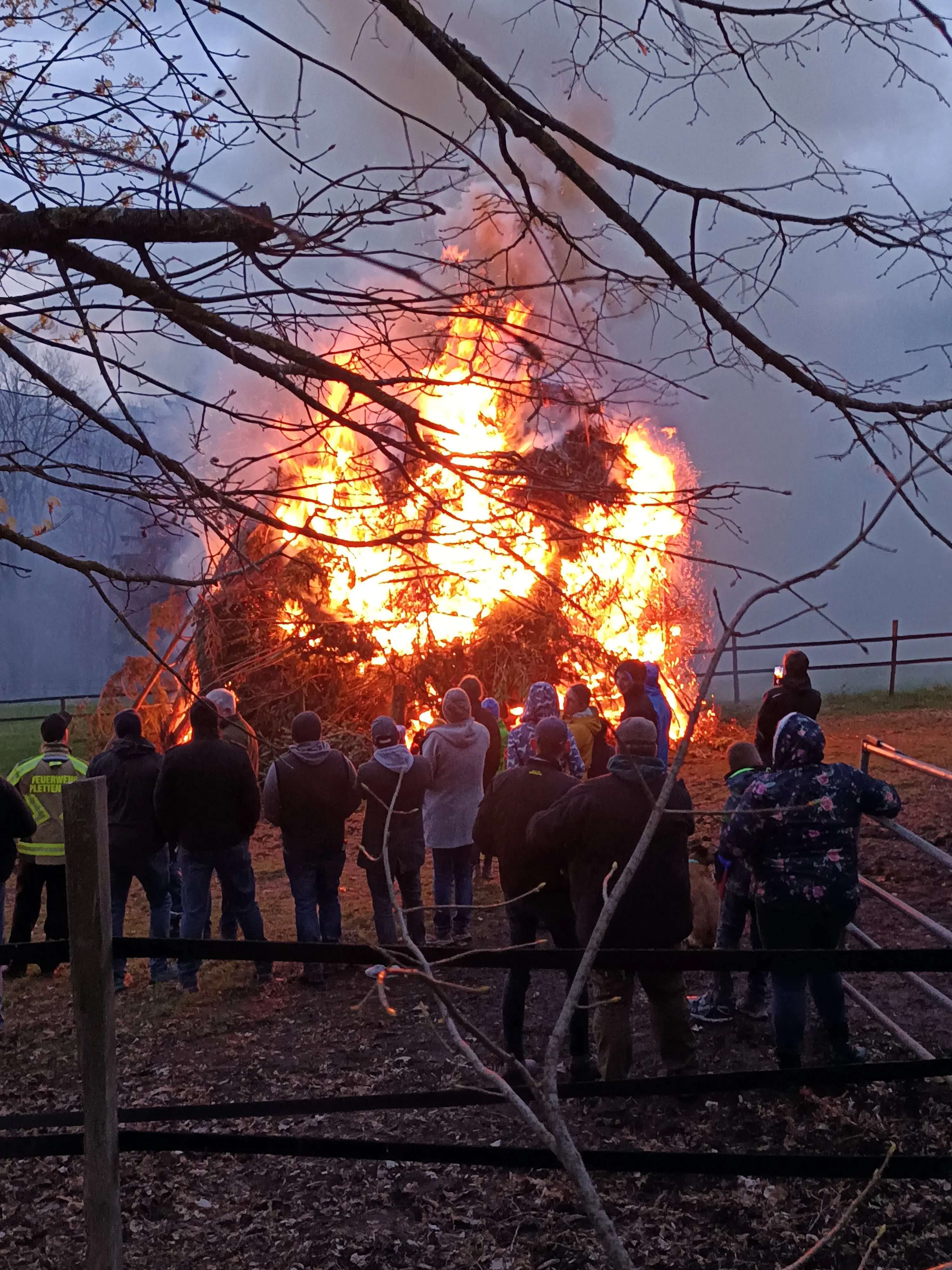 Große Menschenmenge vor einem lodernden Osterfeuer unter einem bewölkten Himmel.