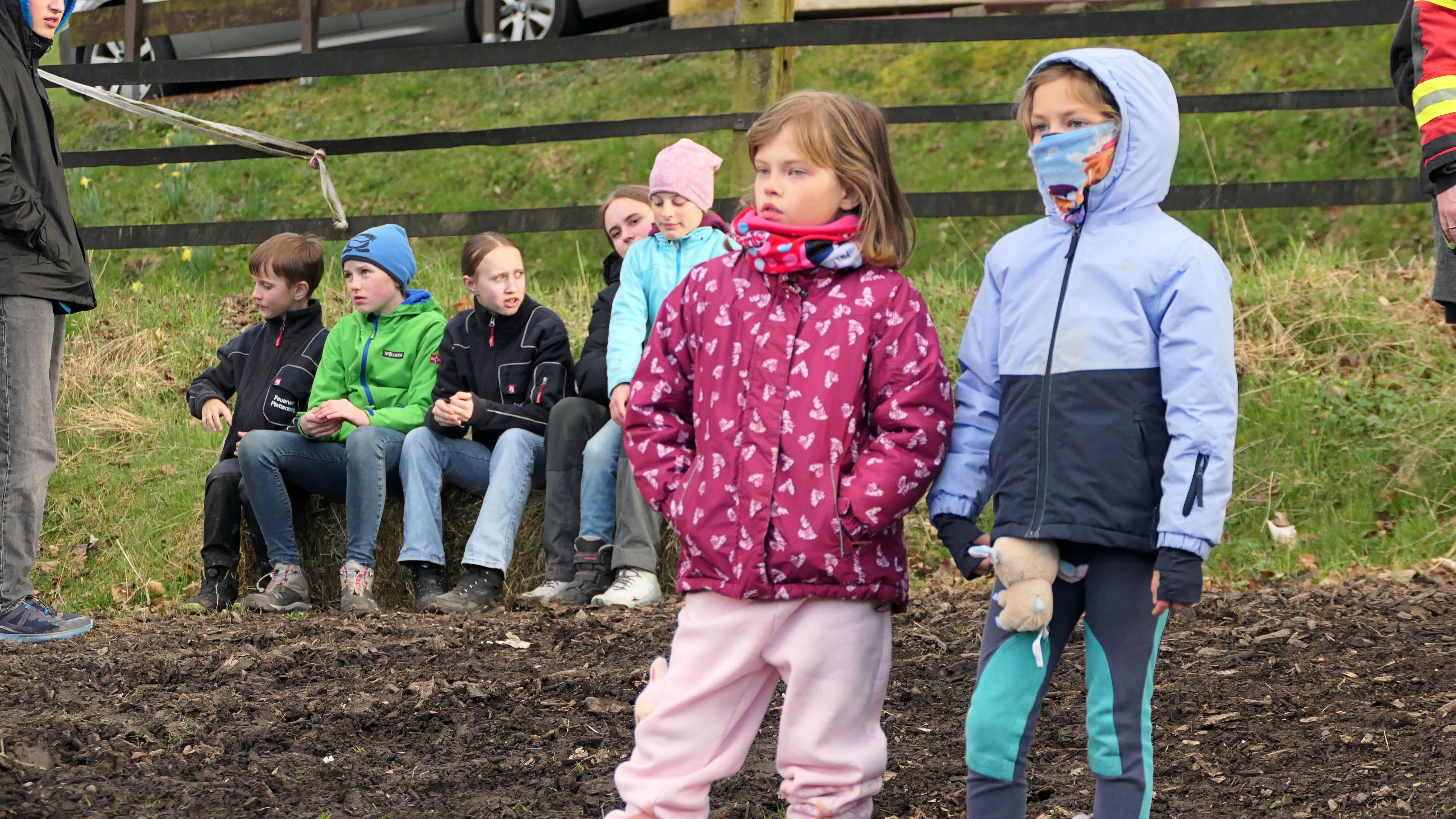 Kinder und Erwachsene stehen und sitzen vor einem großen Holzstapel, der für ein Osterfeuer vorbereitet wurde. Einige Kinder tragen Winterjacken und Mützen.