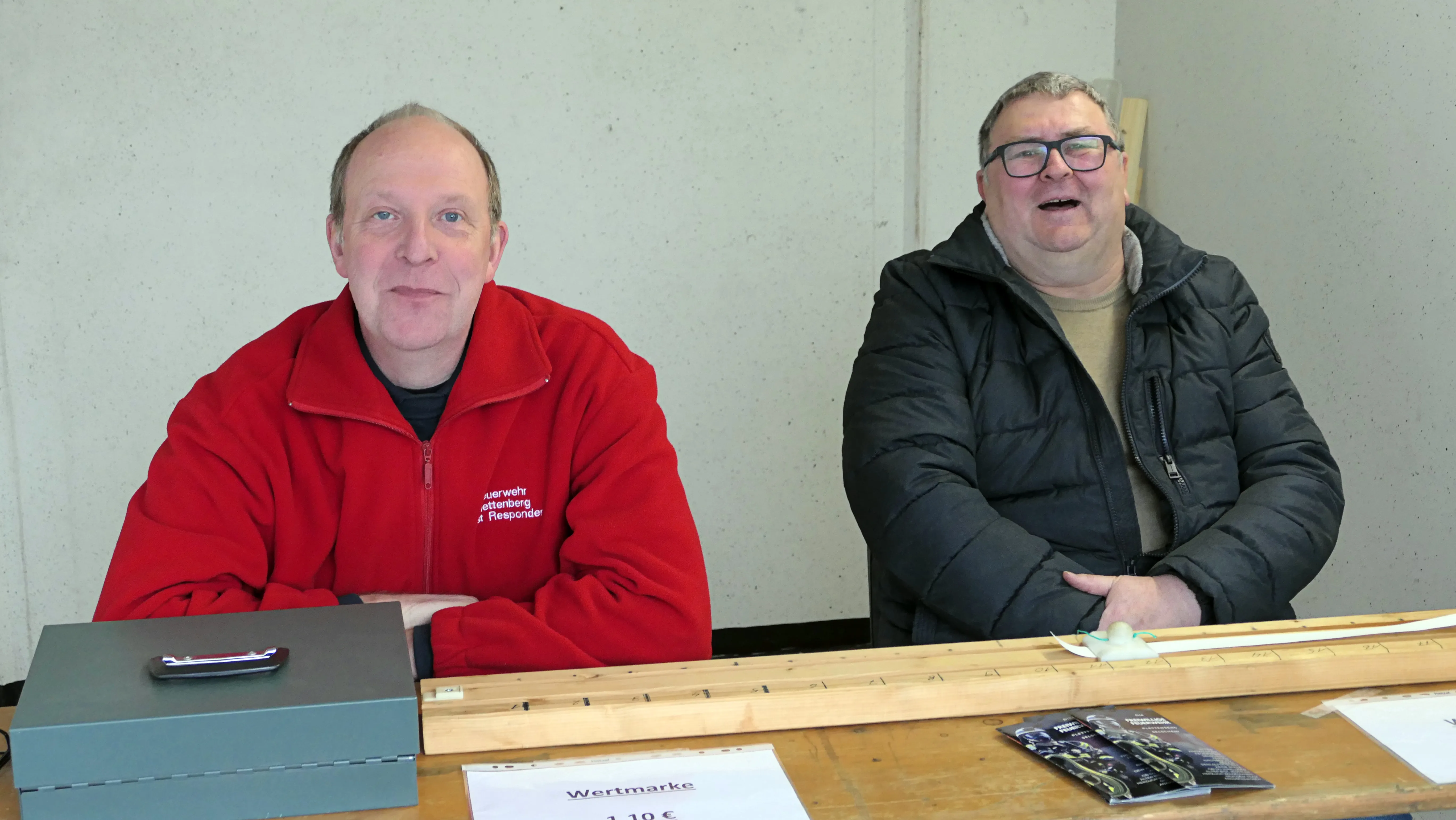 Zwei Männer sitzen an einem Tisch mit Wertmarken und bedienen Besucher des Osterfeuers in Selscheid.