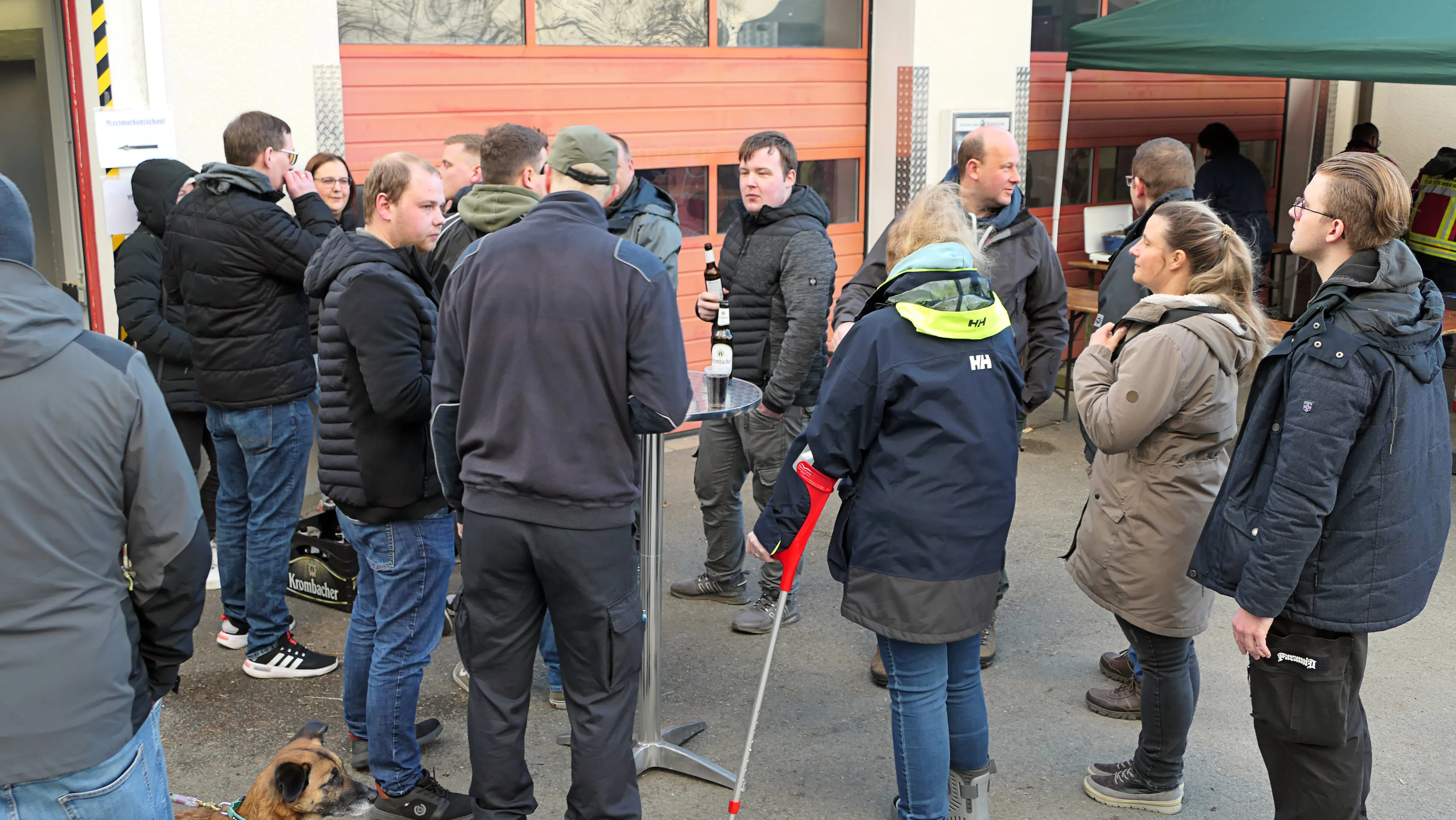 Menschen stehen und unterhalten sich vor einer roten Fahrzeughalle während des Osterfeuers in Selscheid.