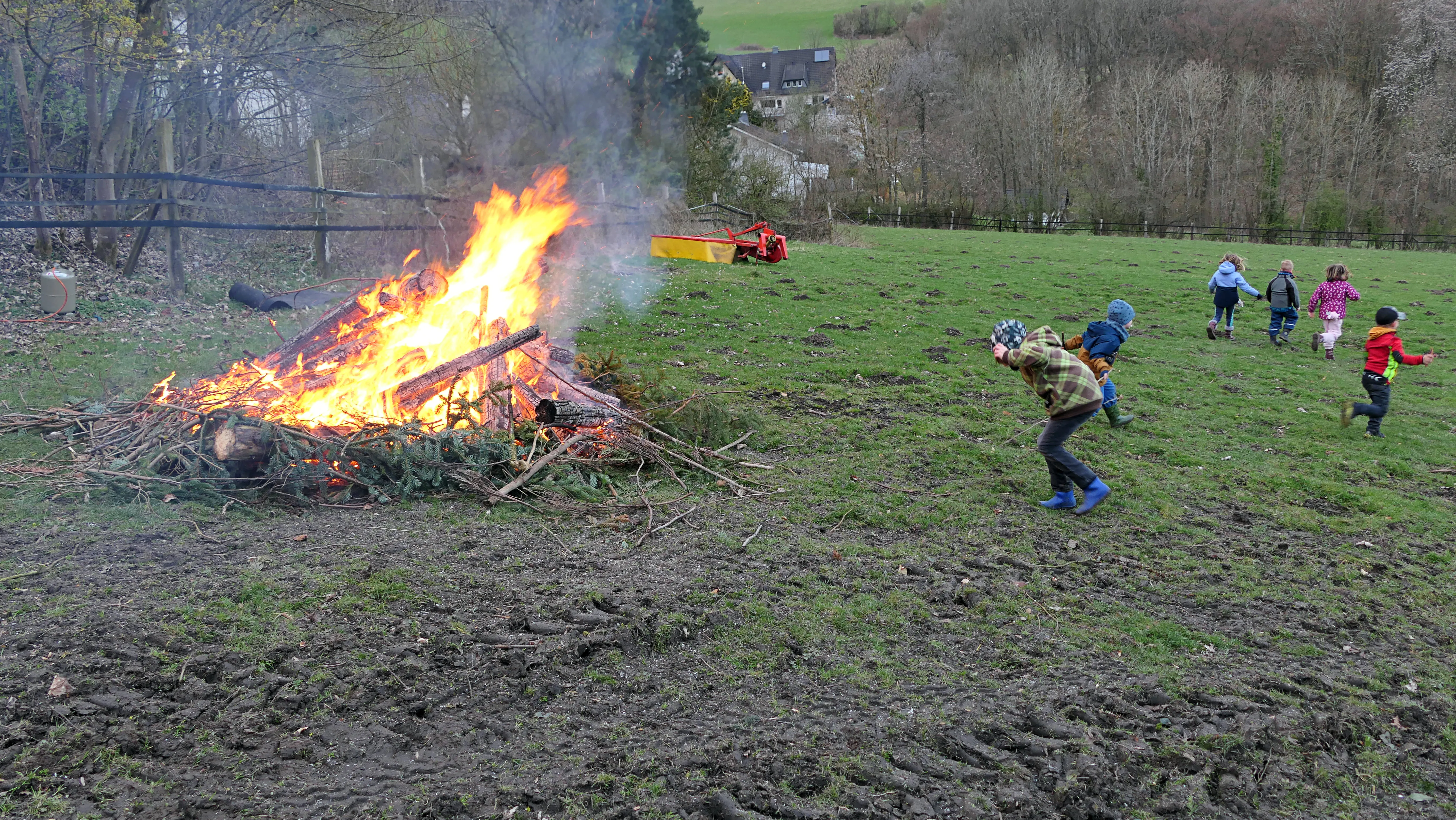 Ein großes Osterfeuer brennt auf einer Wiese, während Kinder umherlaufen und spielen.
