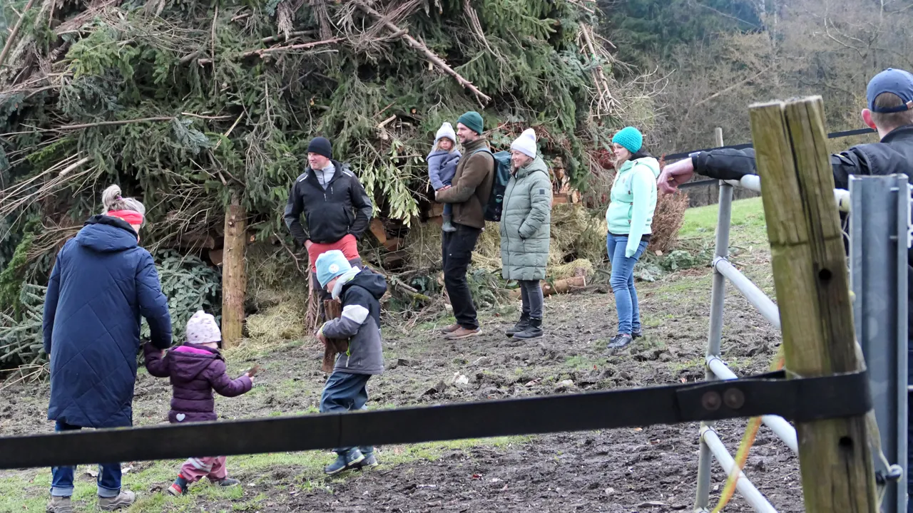 Eine Gruppe von Menschen steht und steht vor einem großen Haufen Ästen und Zweigen, vermutlich für ein Osterfeuer. Kinder spielen im Vordergrund.