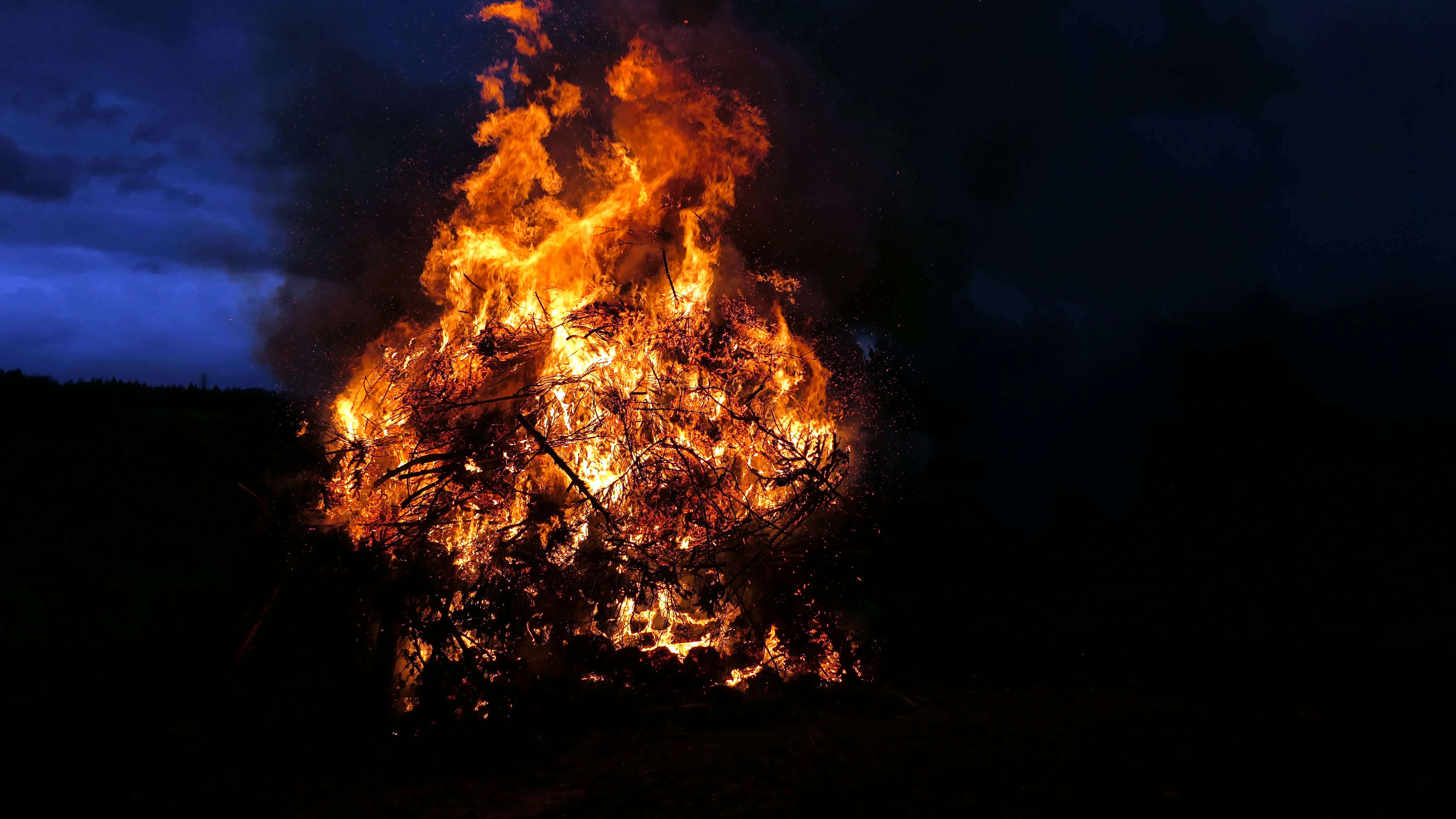 Hohes Osterfeuer mit lodernden Flammen und Funkenflug vor dunklem Himmel.
