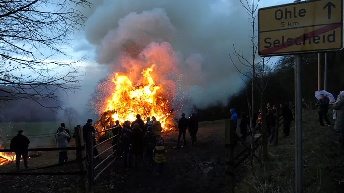 Großes Osterfeuer mit vielen Zuschauern, im Hintergrund ein Wegweiser nach Ohle und Selscheid.