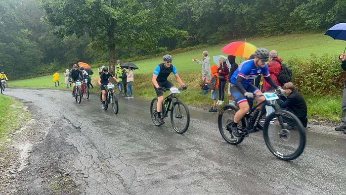 Radfahrer auf einer nassen Straße während eines Radrennens in einer bewaldeten Landschaft.
