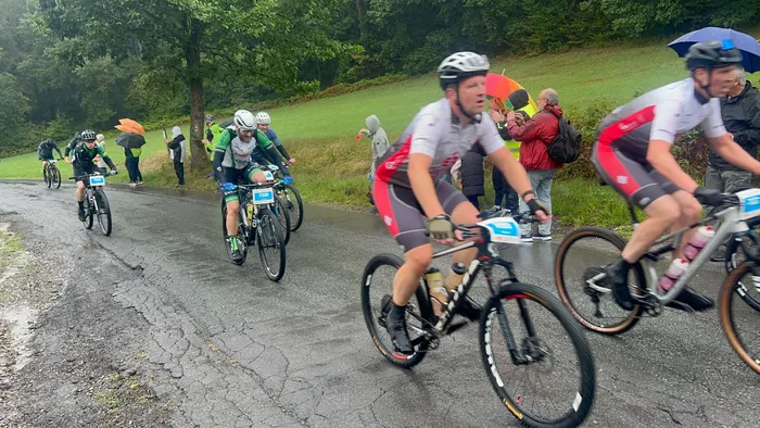 Radfahrer fahren auf einer nassen Straße durch eine bewaldete Hügellandschaft bei Regen.