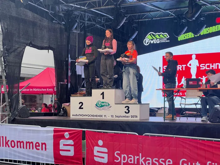 Drei Personen stehen auf einem nummerierten Siegerpodium bei der Siegerehrung des P-Weg-Marathonwochenendes 2026.