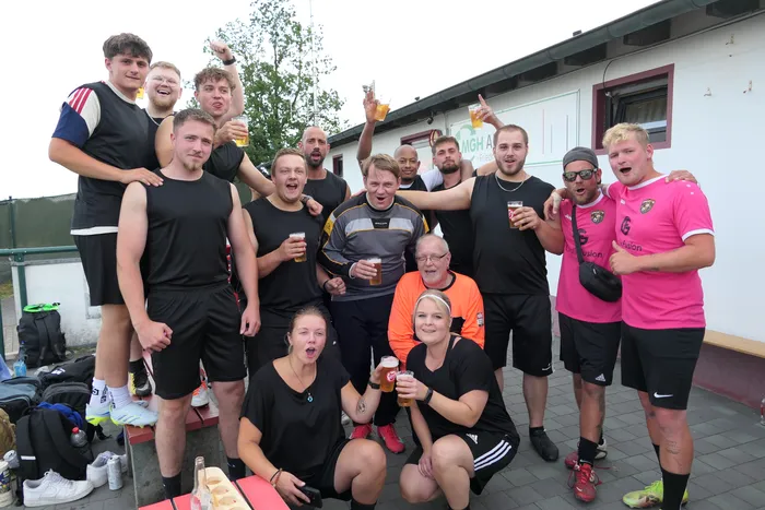 Eine Gruppe von Menschen in Sportkleidung posiert lächelnd mit Getränken bei einem Hobby-Fußballturnier.