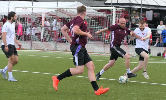 Fußballspieler in weinroten und weißen Trikots kämpfen bei einem Turnier um den Ball auf einem Rasenplatz.