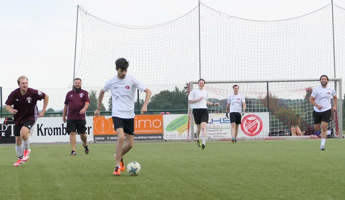 Ein Spieler in einem weißen T-Shirt dribbelt einen Fußball auf einem Rasenplatz während eines Hobby-Fußballturniers.