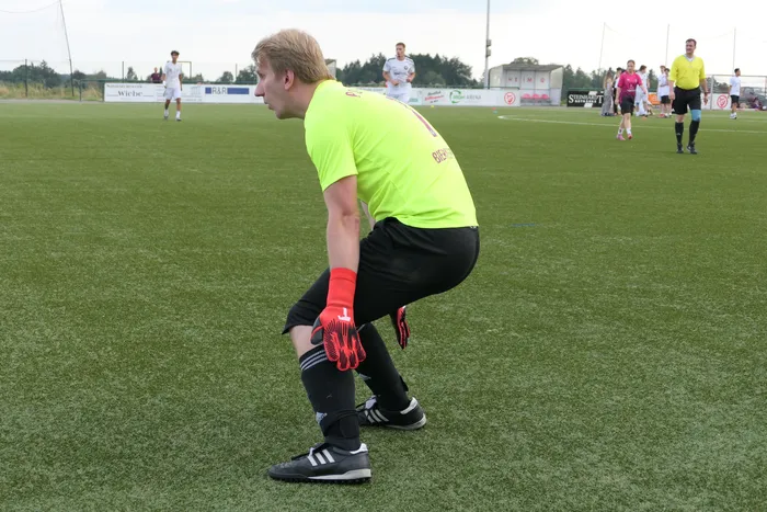 Ein Fußballtorwart in neongelbem Trikot und roten Handschuhen steht in Bereitschaft auf einem Kunstrasenplatz.