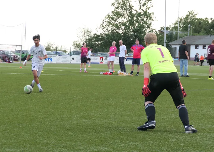 Ein Spieler in weißem Trikot dribbelt den Ball auf einen Torwart in neongelbem Trikot zu.
