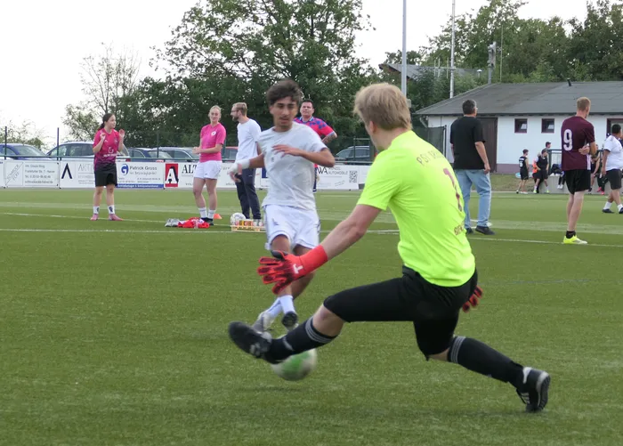 Ein Spieler in einem neongelben Trikot springt bei einem Fußballturnier nach dem Ball, während ein Spieler in Weiß daneben läuft.