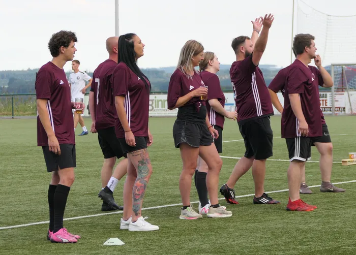 Personen in weinroten Sporttrikots stehen auf einem Fußballplatz während eines Hobby-Fußballturniers.