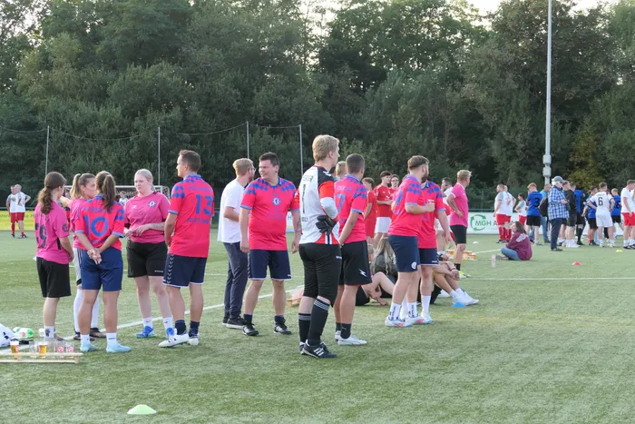 Fußballspieler in roten und blauen Trikots stehen auf einem Kunstrasenplatz.