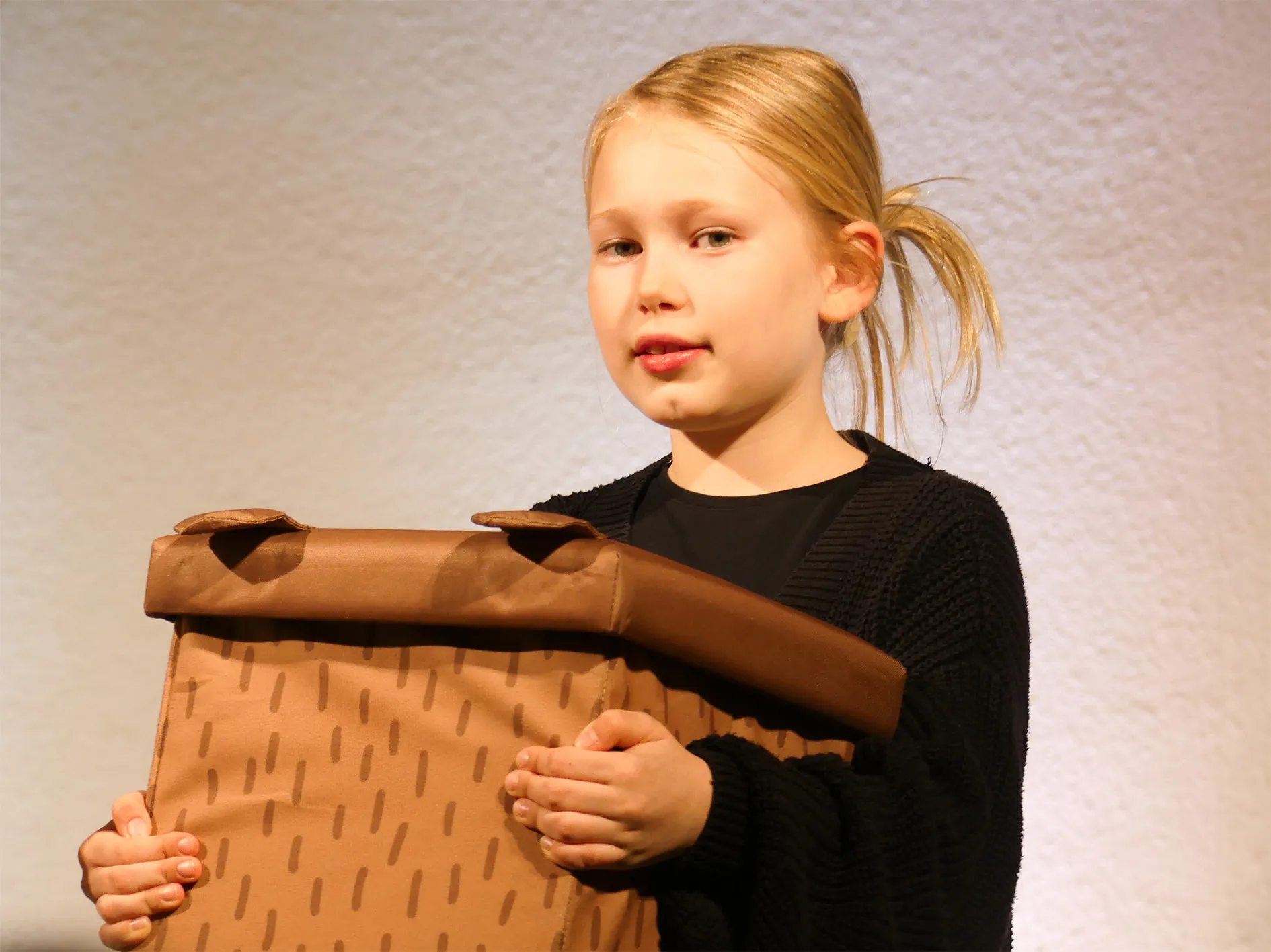 Ein Mädchen hält eine selbstgebastelte Rolle, die als Requisite für das Theaterstück „Der kleine Tag“ dient.