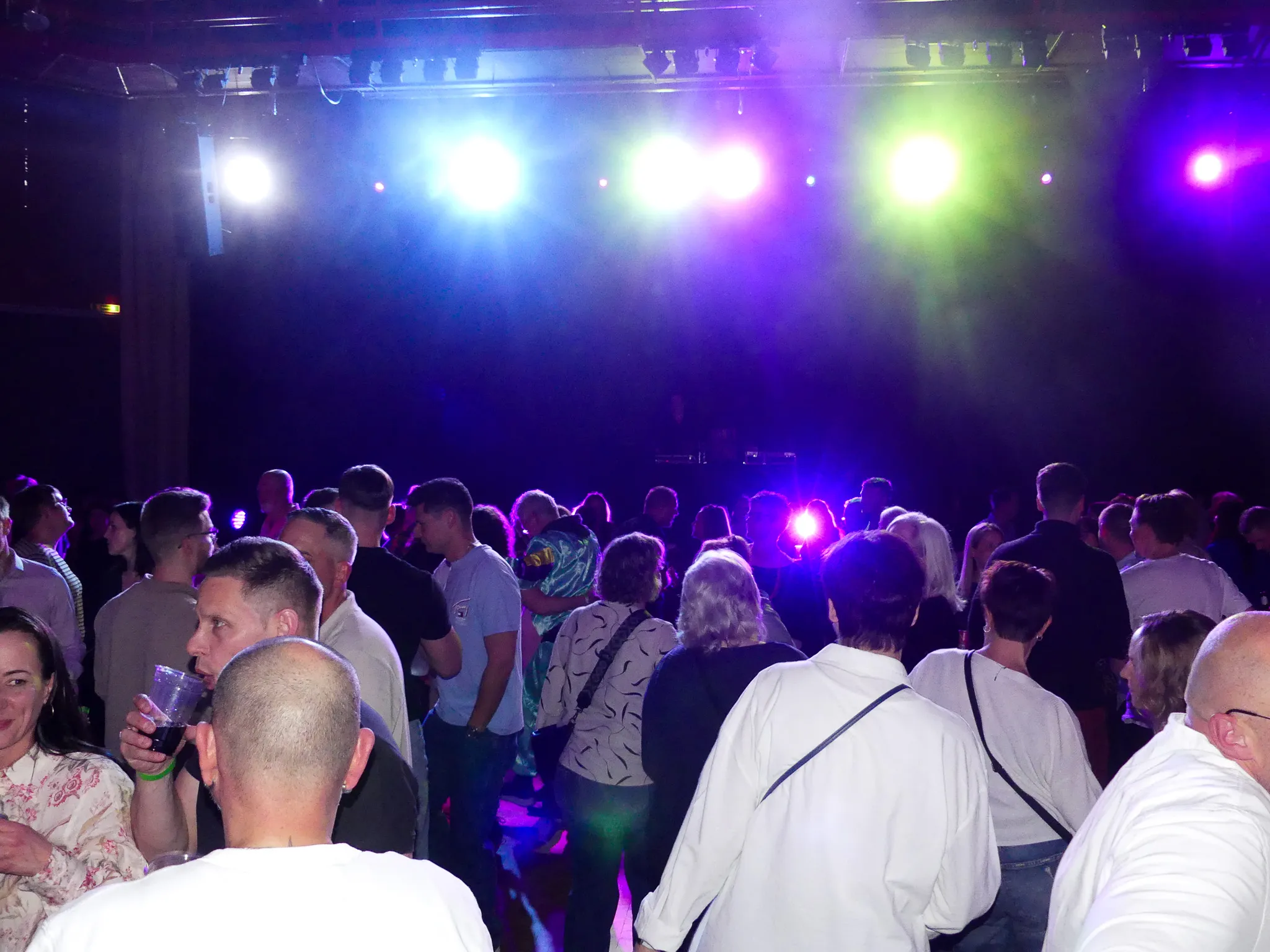 Tanzende Menschen in einem dunklen Raum mit Bühnenbeleuchtung in Lila und Grün.