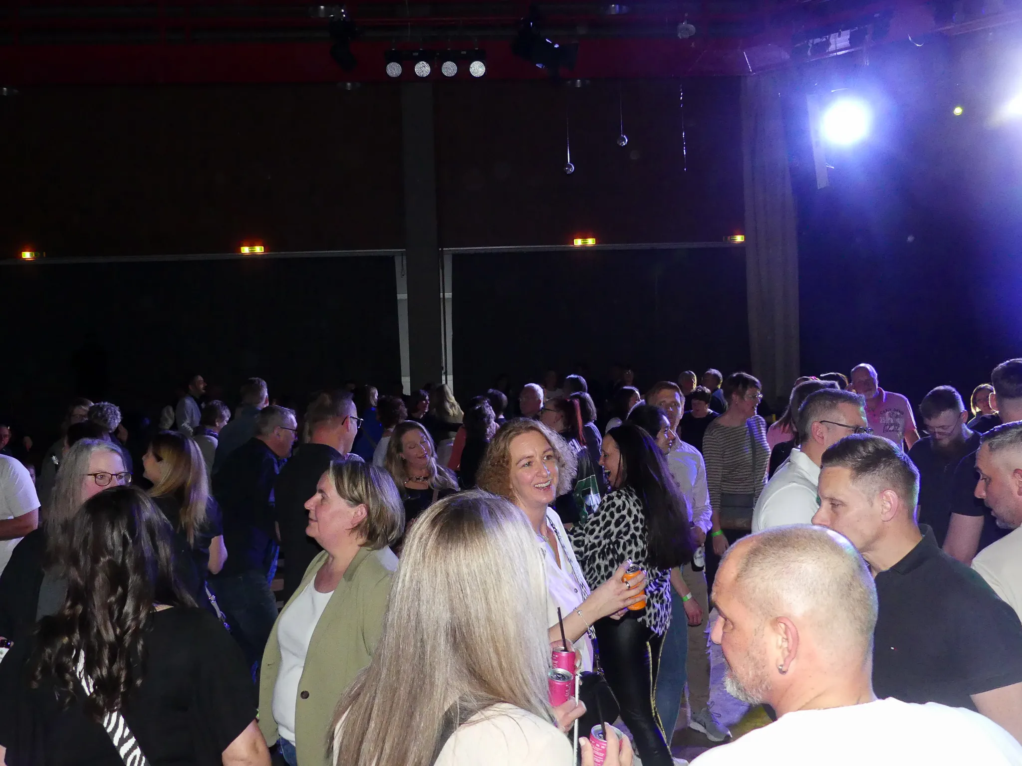 Tanzende Menschen unterschiedlichen Alters auf einer 80er-/90er-Party in Kierspe, viele lächeln und halten Getränke in der Hand.