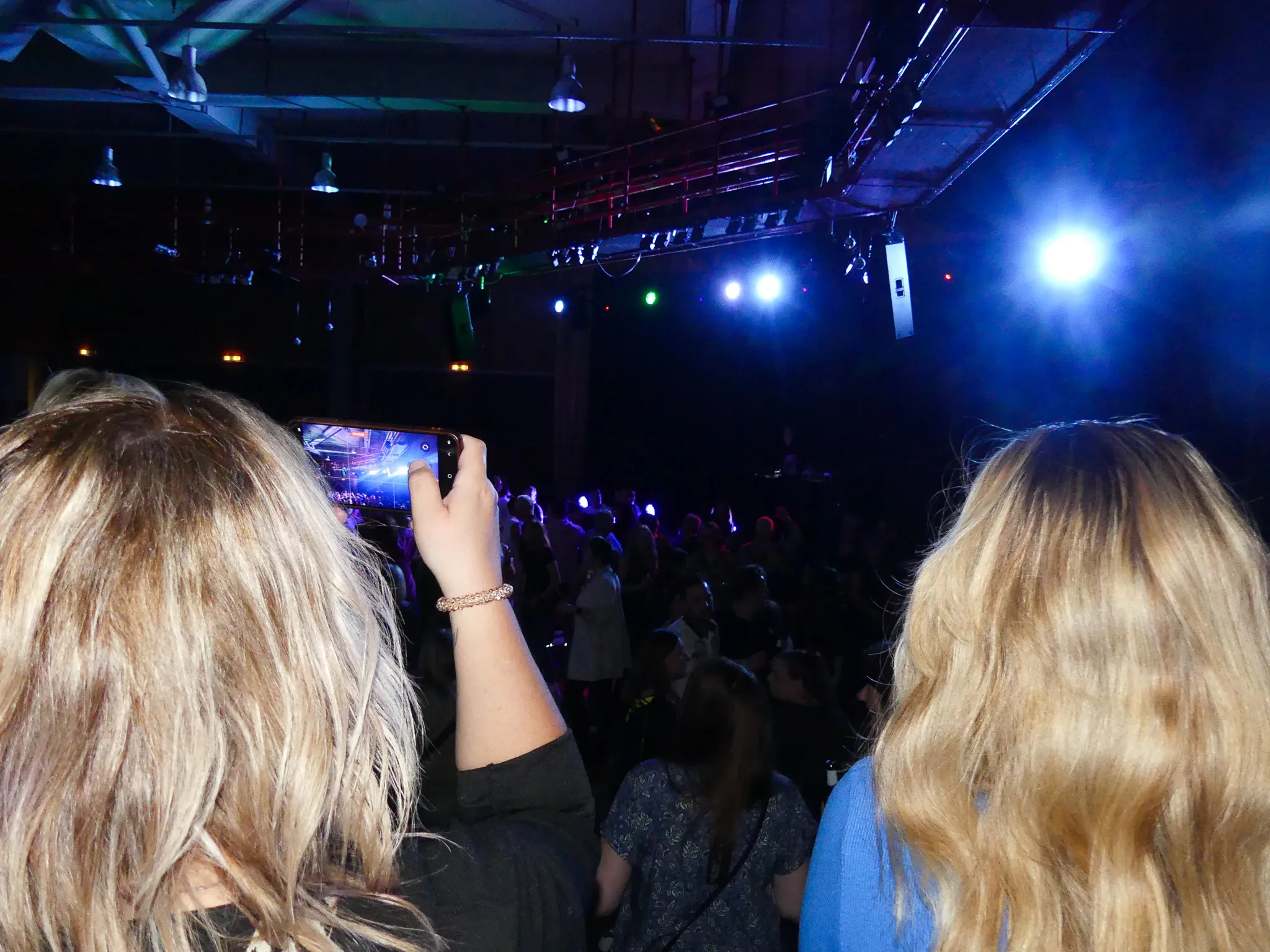 Eine Person filmt mit dem Smartphone die tanzende Menge auf einer 80er-/90er-Party in Kierspe. Im Hintergrund sind Scheinwerfer und Bühnentechnik zu sehen.