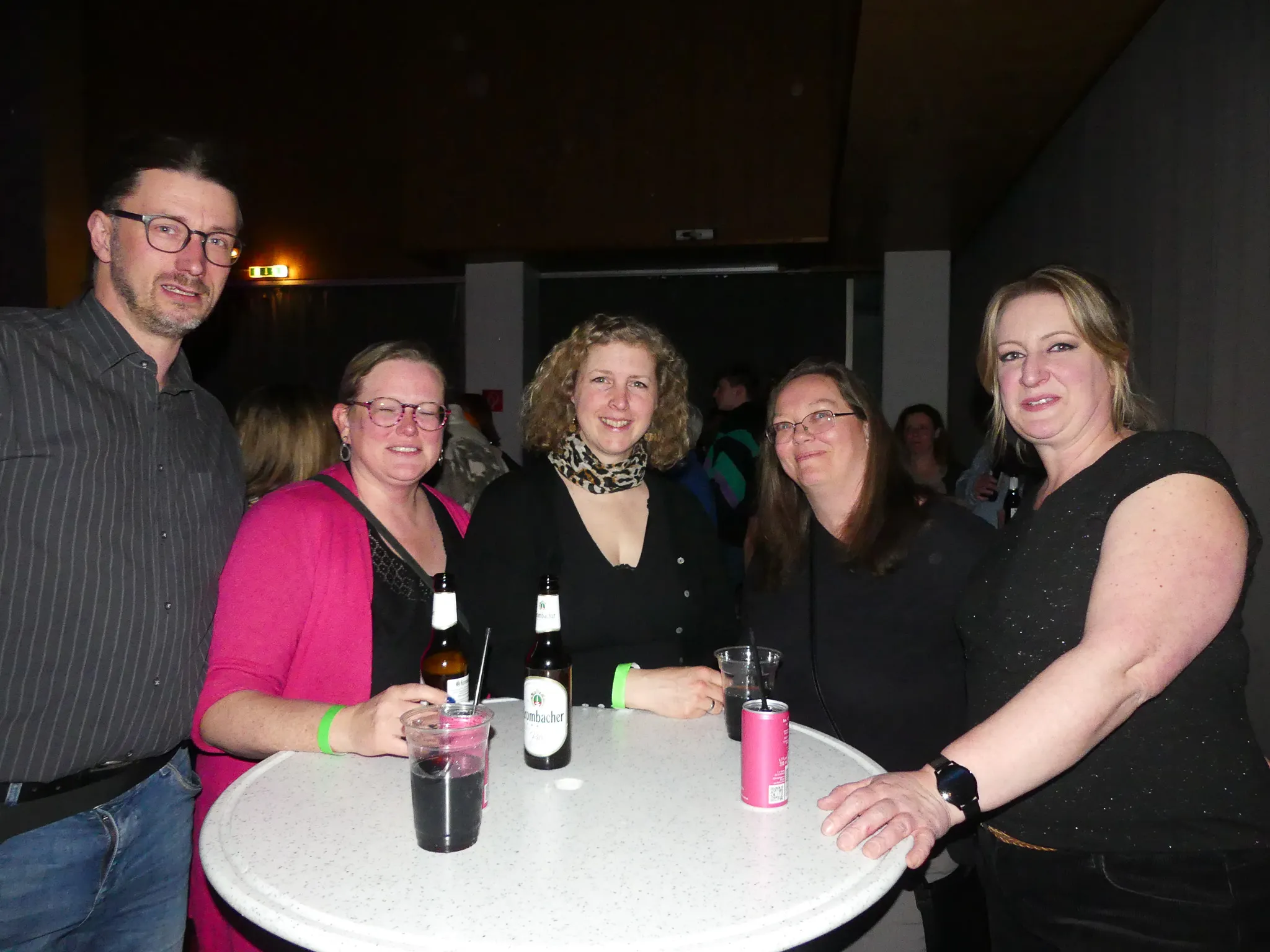 Fünf lächelnde Menschen stehen um einen runden Tisch mit Getränken auf einer 80er-/90er-Party in Kierspe.