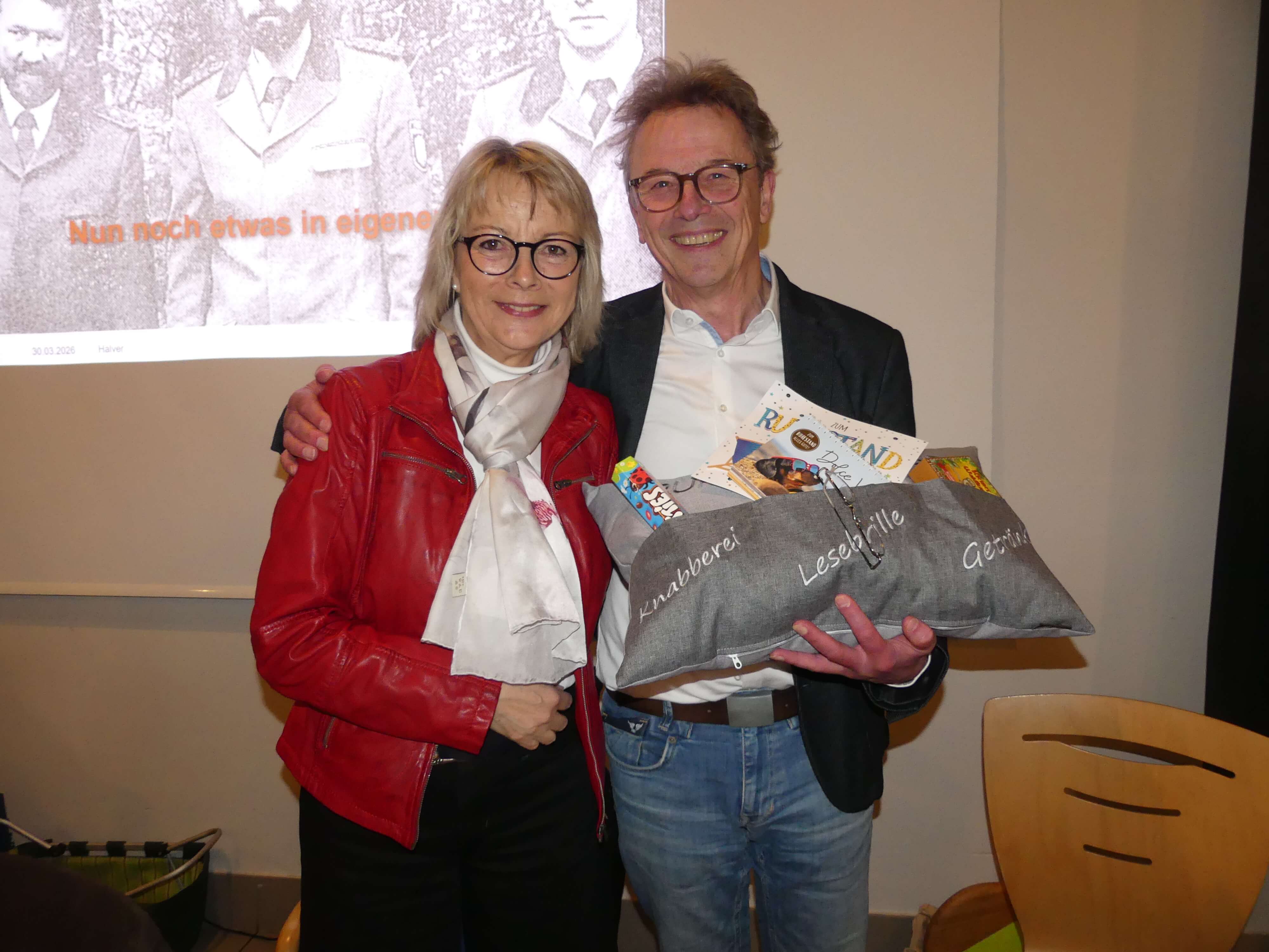 Astrid Becker und Förster Uli Ackfeld umarmen sich bei Ackfelds Verabschiedung aus dem Dienst. Ackfeld hält ein Kissen mit Aufschriften wie „Knabberei“ und „Lesebrille“.