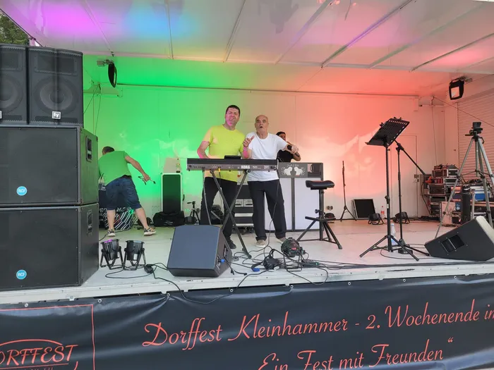 Drei Musiker spielen auf einer Bühne unter einem Zelt. Im Hintergrund ein Banner mit der Aufschrift „Dorfest Klehammer“.