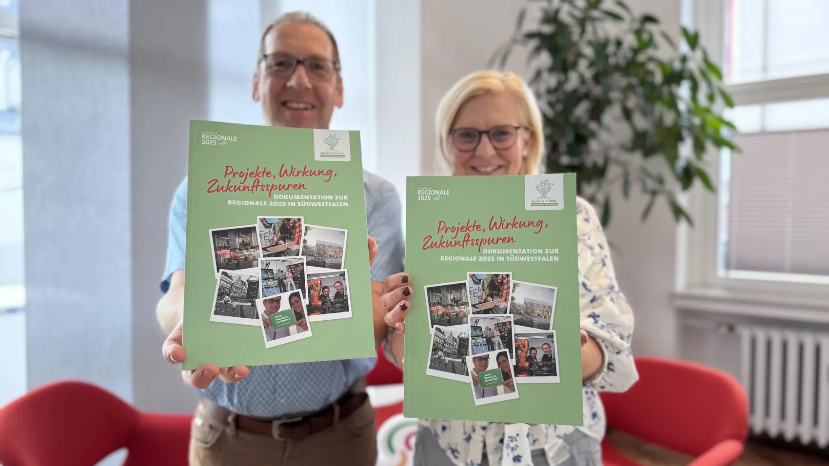 Zwei Personen halten die grüne Dokumentation „Projekte, Wirkung, Zukunftsspuren“ zur Regionale 2025 in Südwestfalen hoch.