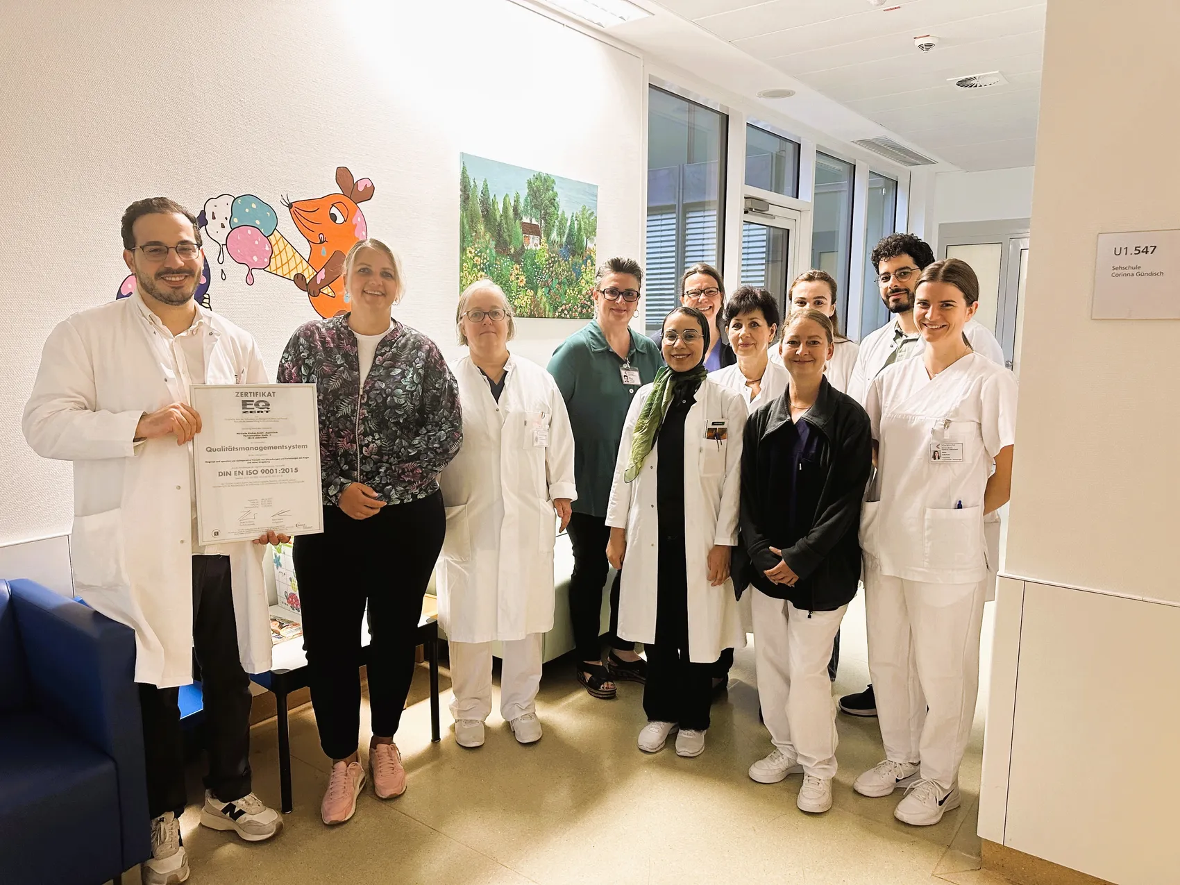 Das Team der Augenklinik posiert gemeinsam und hält ein Zertifikat für die erfolgreiche Re-Zertifizierung nach DIN EN ISO 9001:2015.