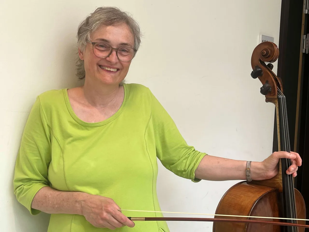 Die Cellolehrerin Dorothee Matthes lächelt und hält einen Bogen sowie den Hals eines Cellos.