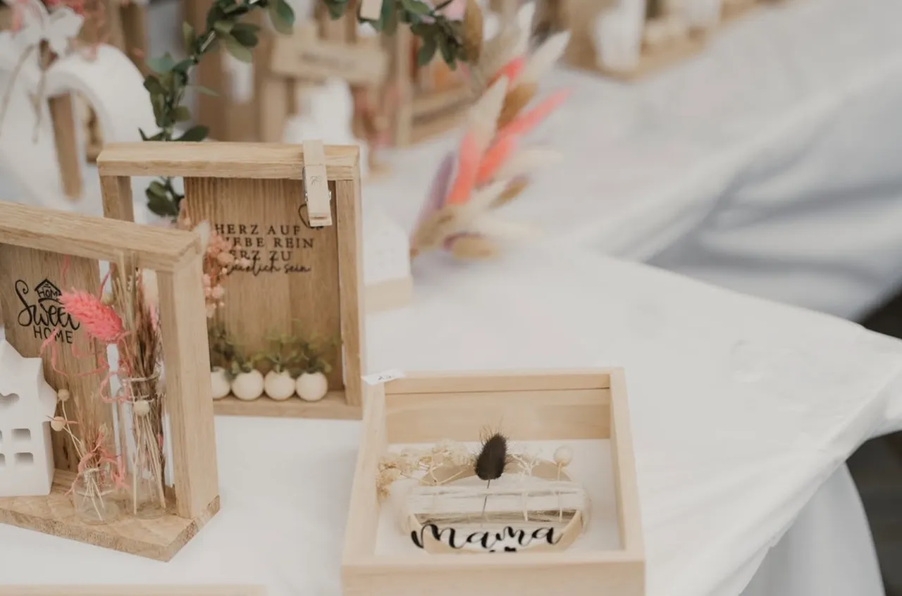 Holzrahmen mit Dekorationen und Schriftzügen wie „Sweet Home“ und „Mama“ stehen auf einem weißen Tisch.