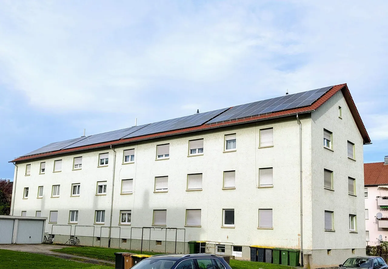 Mehrfamilienhaus mit großflächiger Photovoltaikanlage auf dem Dach, die Solarstrom erzeugt.
