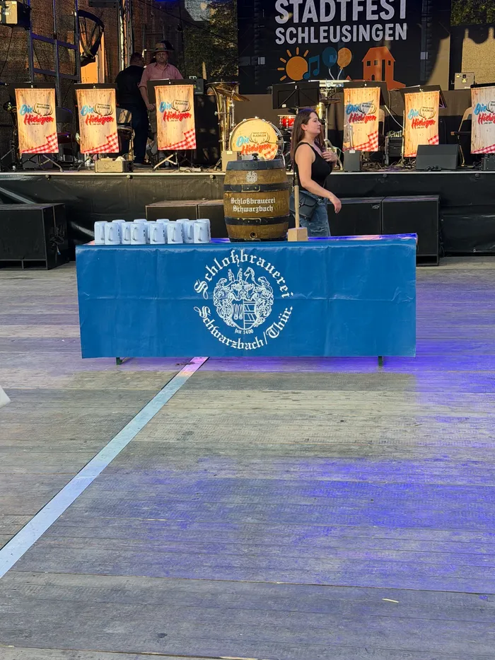 A woman stands behind a table with a beer barrel and logo of 