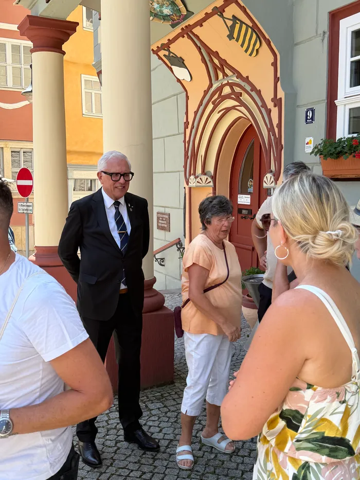 Frank-Michael Schwarz, Bürgermeister von Plettenberg, im Gespräch mit einer Frau vor einem historischen Gebäude in Schleusingen. Im Hintergrund weitere Personen und ein mit Blumen geschmückter Balkon.