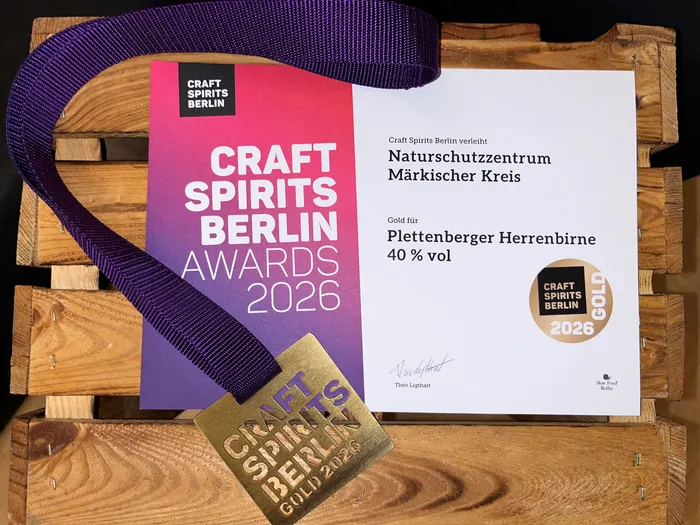 Goldene Auszeichnung des Craft Spirits Berlin Awards 2026 für Plettenberger Herrenbirne, präsentiert auf einer Holzpalette mit einem violetten Band.