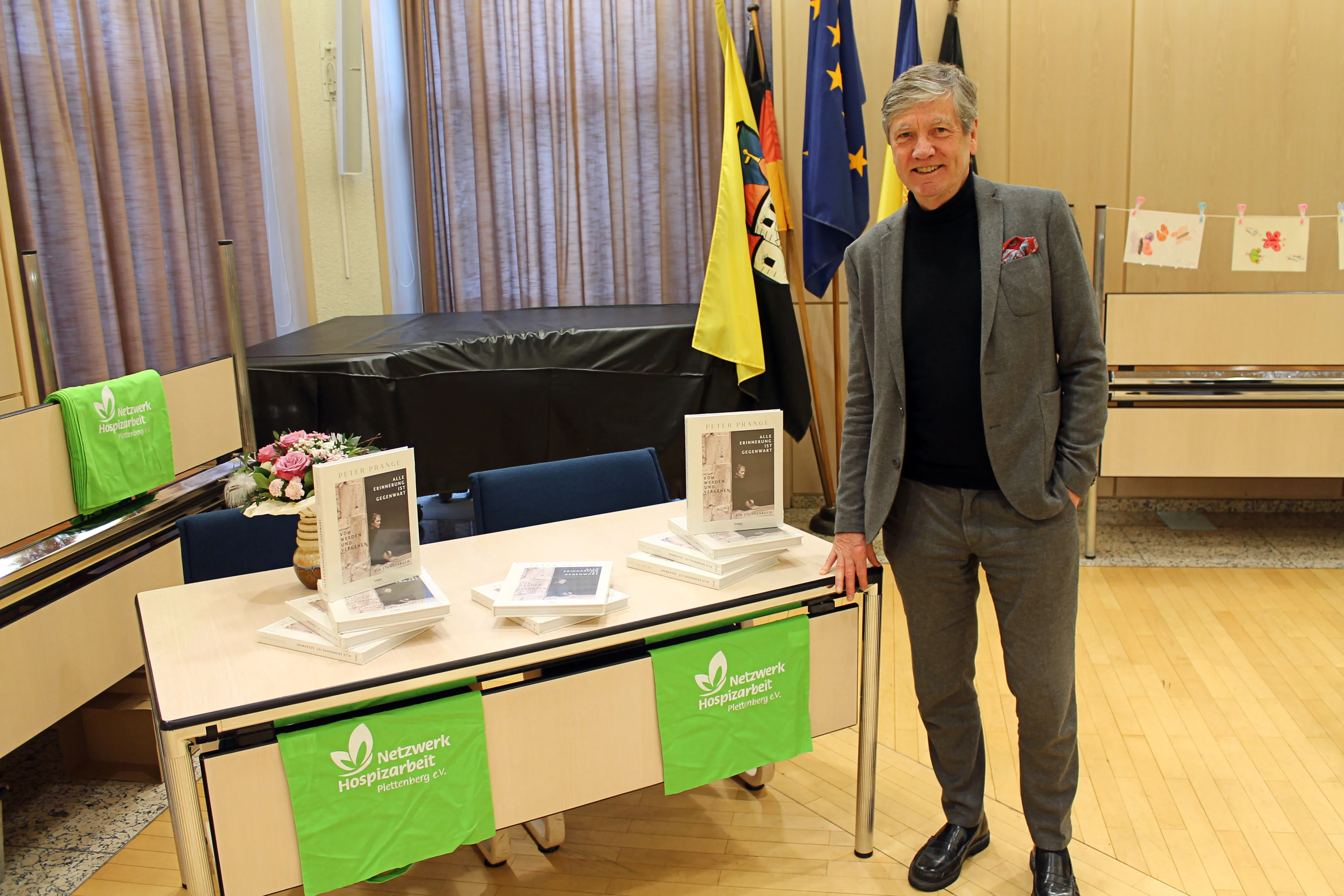Ein Mann in einem grauen Anzug steht lächelnd neben einem Tisch mit Büchern und Werbematerialien für das Netzwerk Hospizarbeit Plettenberg.