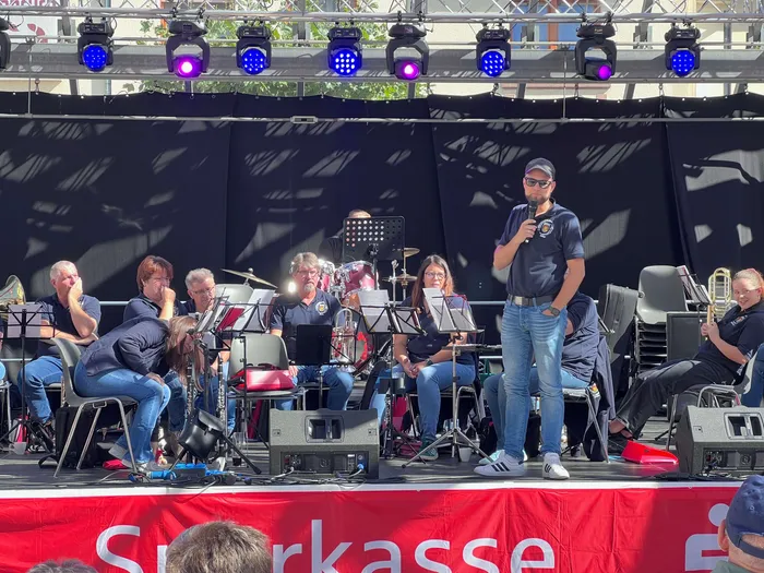 Marvin Schädle spricht in ein Mikrofon auf einer Bühne vor den Musikern des Feuerwehr-Musikzugs.
