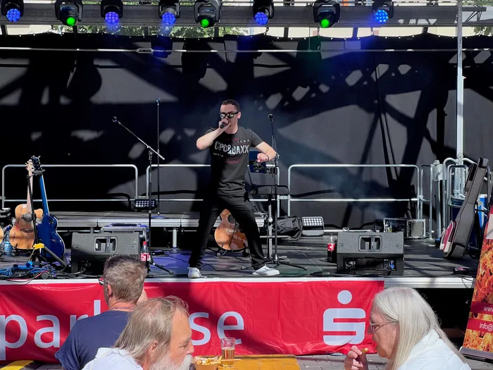 Ein Mann mit Sonnenbrille singt auf einer Bühne bei einem Stadtfest.