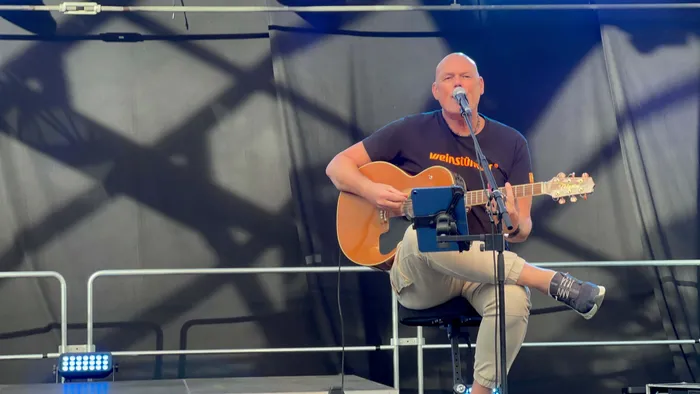 Ein Mann spielt Akustikgitarre und singt in ein Mikrofon auf einer Bühne bei einem Stadtfest.