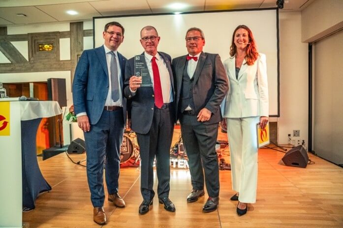 Burkard Kaiser nimmt den E-Markenpartner-Ehrenpreis 2026 entgegen, überreicht von Stefan Ehinger und Olaf von Müller. Moderatorin Anja Lange steht neben dem Preisträger.