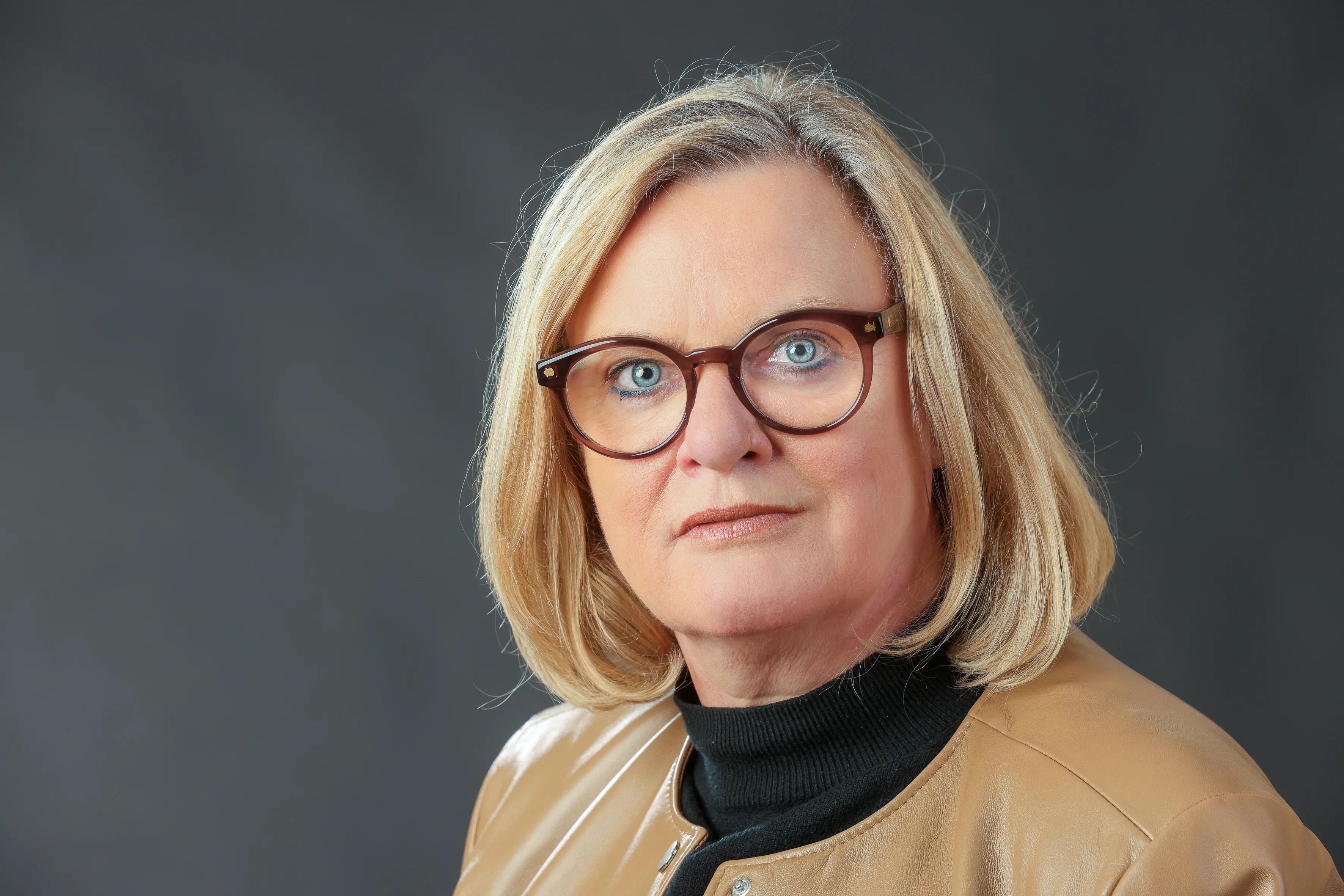 Porträt von Kirsten Stich, Landtagsabgeordneter aus dem Ennepe-Ruhr-Kreis, mit blondem Haar und Brille vor grauem Hintergrund.