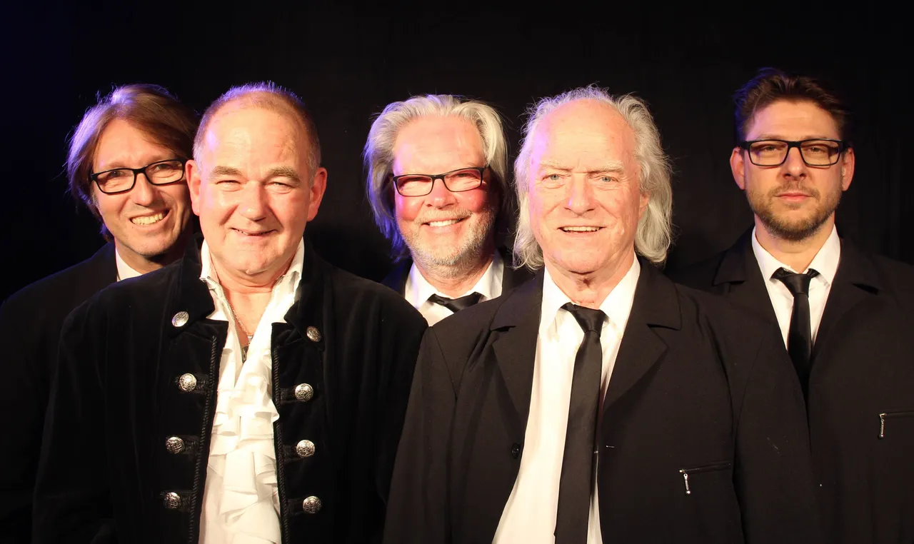 Fünf Männer mittleren und höheren Alters posieren lächelnd für ein Porträt. Der Mann in der Mitte trägt eine traditionelle Jacke mit silbernen Knöpfen.