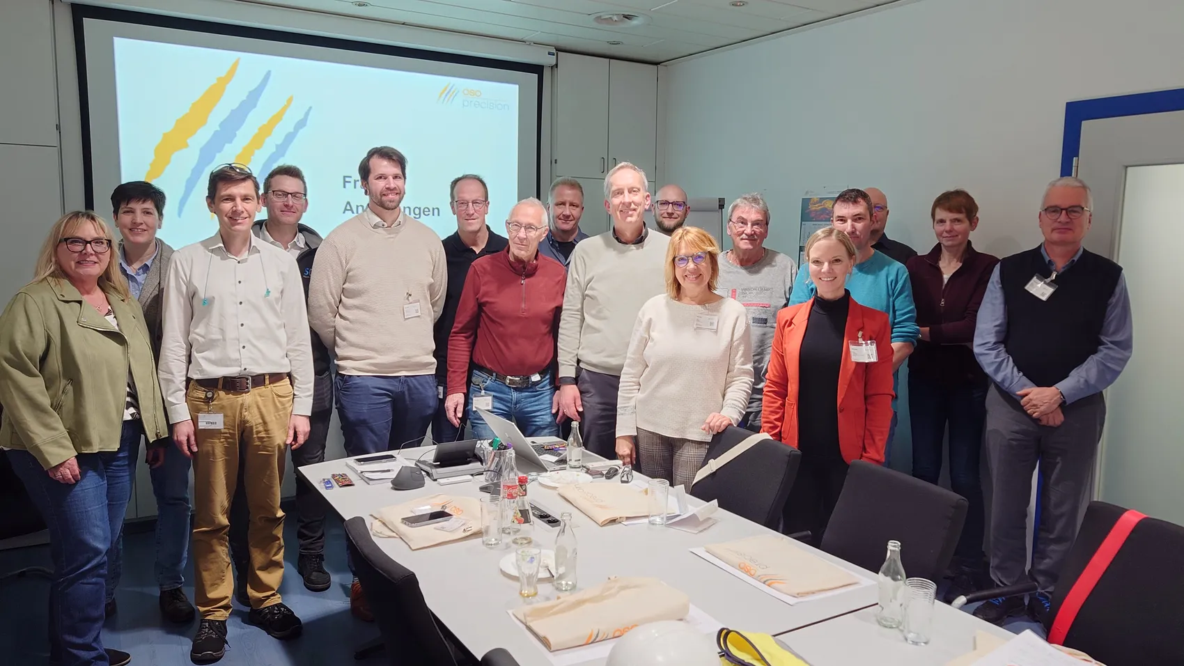 Gruppe von etwa 20 Fachleuten für Qualitätsmanagement posiert in einem Konferenzraum vor einer Präsentation mit dem Logo von oso precision.