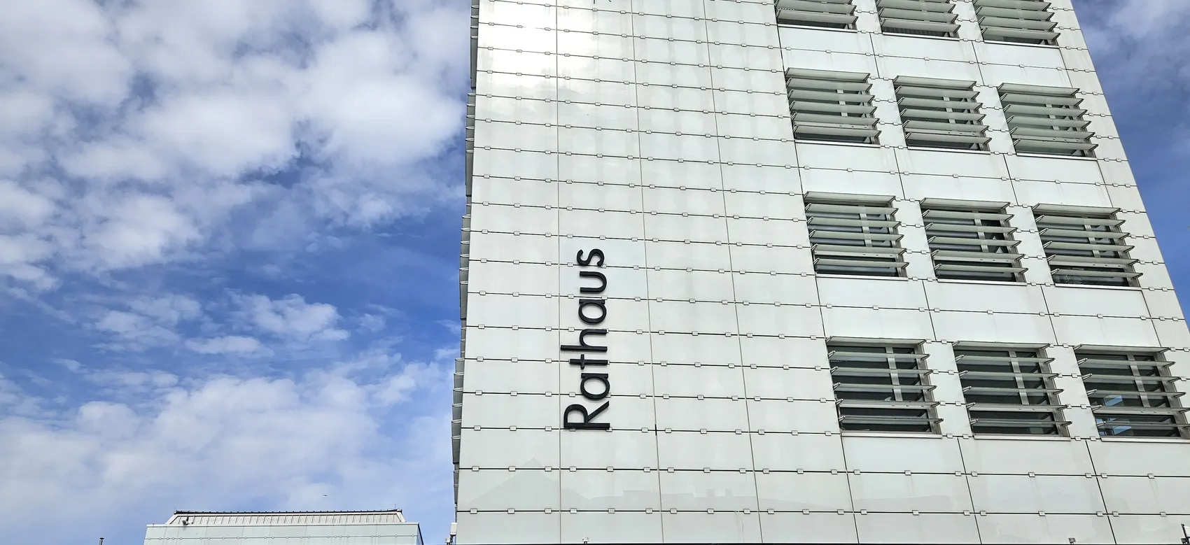 Das Rathaus mit dem Schriftzug „Rathaus“ an der Fassade, vor blauem Himmel mit Wolken.