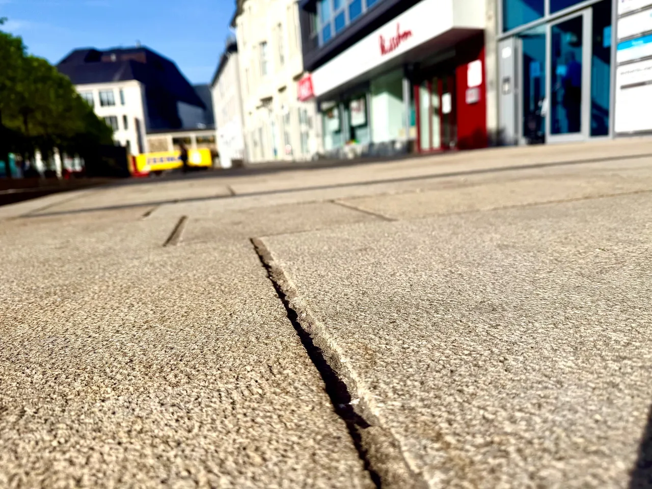 Nahaufnahme einer Fuge im Pflaster des Rathausplatzes, im Hintergrund Gebäude mit Geschäften.