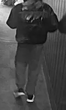 Rückansicht einer Person mit dunkler Kleidung und hellen Schuhen, die eine Tasche trägt.